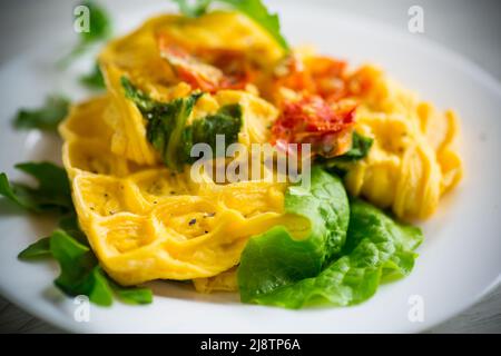 Omelette aux œufs farcie à la tomate et aux légumes verts frits sous forme de gaufres, sur une table en bois. Banque D'Images