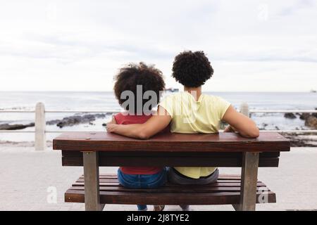Vue arrière d'un jeune couple afro-américain qui regarde la mer tout en étant assis sur un banc Banque D'Images