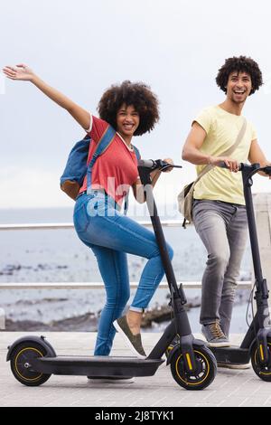 Portrait d'un jeune couple afro-américain heureux avec des scooters de poussée contre le ciel, espace de copie Banque D'Images