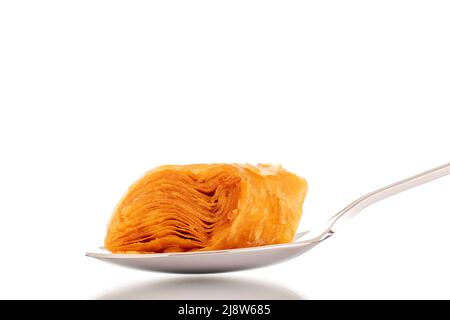 Une tranche de baklava au miel sucré avec une cuillère en métal, en gros plan, isolée sur fond blanc. Banque D'Images