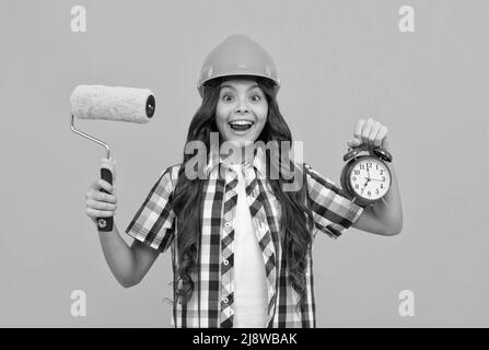 surprise adolescente tenir le rouleau de peinture et le réveil. enfant dans le casque. temps pour la décoration. Banque D'Images