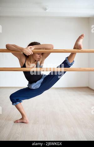 Jeune danseuse flexible qui s'étire les jambes sur la barre de ballet dans la salle de danse Banque D'Images