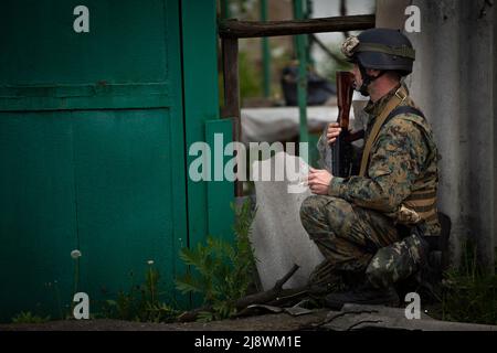 Barvinkove, Kharkiv Oblast, Ukraine. 18th mai 2022. Aaron, soldat vétéran, regarde à travers un trou dans la clôture pour appeler un chien qui vit dans une maison endommagée par des bombardements à Barvinkove, en Ukraine, le 18 mai 2022. Aaron, qui combat depuis 14 jours aux lignes de front près d'Izyum, va bientôt à Kiev pour recevoir un traitement médical pour son dos. Il a décidé de montrer la nouvelle recrue Yost, pas en photo, la destruction dans la ville et lui apprendre à reconnaître les obus entrants et sortants. Crédit : ZUMA Press, Inc./Alay Live News Banque D'Images