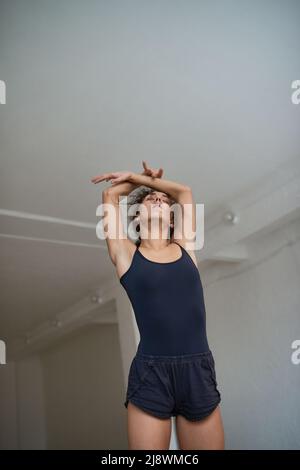 Vue à angle bas d'une jeune femme mince qui s'étire avec les yeux fermés dans un studio de danse Banque D'Images