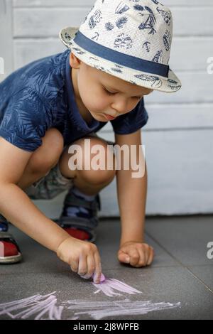 Un garçon dessine avec des crayons sur l'asphalte . Peinture. Jeux d'été dans la rue. Divertissement et loisirs pour les enfants. L'enfant met beaucoup d'effort et le Banque D'Images