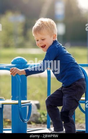 Enfant en fête. Garçon tourne sur le carrousel pour les enfants sur le terrain de jeu. Un jeune garçon joue seul. Enfant en chandail bleu aux cheveux blonds. Guy est Banque D'Images