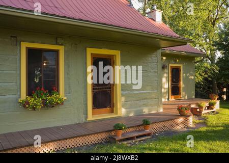 Vieux vers 1840 maison en rondins vernie vert olive style cottage Canadiana avec garniture jaune et toit en tôle marron. Banque D'Images