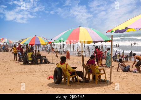 Touristes se détendre après un bain sous un parapluie à la plage de Puri à Odisha, Inde Banque D'Images