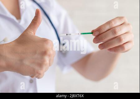 Une femme médecin sans visage tient un test de grossesse rapide négatif. Gynécologue dans un pelage médical et avec un stéthoscope tient le pouce vers le haut. Non désiré Banque D'Images