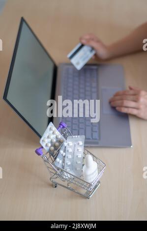 Concept de pharmacie en ligne. Une femme tient une carte de débit dans ses mains et achète des pilules en ligne. Une fille fait un achat en ligne de médicaments avec la maison Banque D'Images