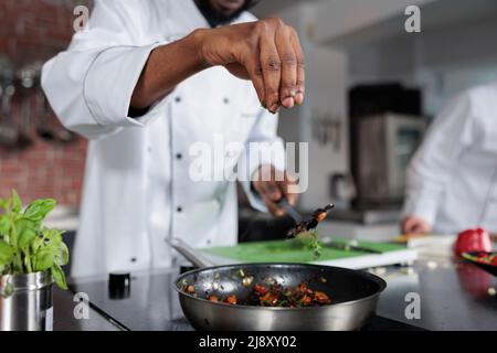 Plat d'assaisonnement du chef principal préparé pour un concours de nourriture organisé dans un restaurant gastronomique. Chef cuisinier lancer des herbes fraîches hachées dans la casserole pour améliorer le goût du repas pendant que dans la cuisine professionnelle. Banque D'Images