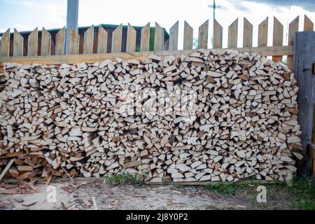 Le bois de chauffage est empilé dans une pile de bois le long de la clôture contre le ciel bleu. Récolte du bois de chauffage pour le bain et chauffage de la maison Banque D'Images