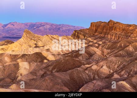 Badlands et la chaîne Panamint s'illuminent avec une douce lumière matinale à Zabriske point, dans le parc national de la Vallée de la mort, en Californie. Banque D'Images