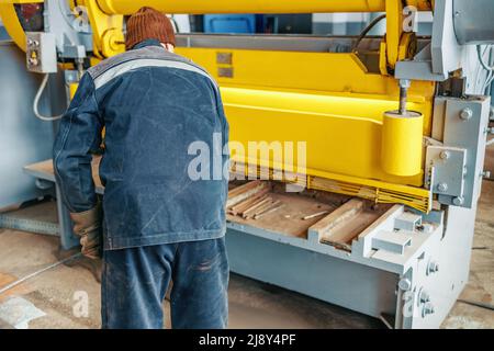 L'ouvrier coupe le métal sur la machine à guillotine mécanique dans le hall de production. Equipement industriel pour la découpe des métaux. Scène réelle. Flux de travail réel. Homme au travail. Banque D'Images