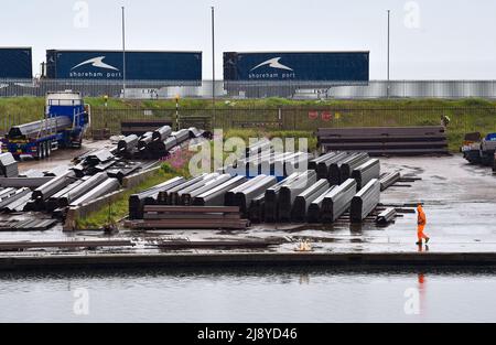 Brighton UK 19th mai 2022 - travailleur portuaire sous la pluie sur un site de stockage d'acier à Shoreham Port , Sussex après une nuit de tonnerre et de foudre le long de la côte sud : Credit Simon Dack / Alamy Live News Banque D'Images