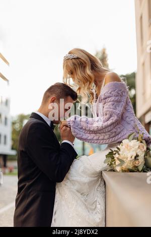 Beau jeune couple de mariage en costume noir et robe blanche promenez-vous dans la ville, baiser et profiter sur fond de rue. Portrait de mariée heureuse avec Banque D'Images