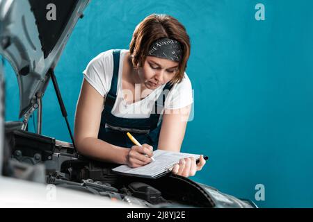 Le portrait d'une femme mécanicien en combinaison signe les documents au service de réparation automobile. Le concept de l'égalité de la femme et travaille à l'atelier de réparation automobile. Banque D'Images