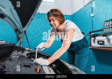 Mécanicien femme en combinaison réparer un moteur avec clé à cliquet. Le concept de l'égalité de la femme et travaille à l'atelier de réparation automobile. Banque D'Images