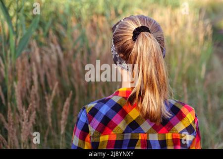 Refocalisation de la coiffure de queue de cheval. Jeune fille ou préadolescente marchant sur fond de nature et se tenant en arrière-plan. Petite fille d'enfant. Prairie verte. Génération z. Automne, Banque D'Images