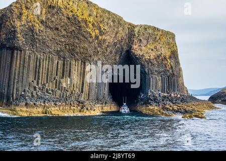 Un bateau touristique se trouve à l'entrée de la grotte de Fingal sur l'île de Staffa, dans les Hébrides intérieures, en Écosse, au Royaume-Uni Banque D'Images