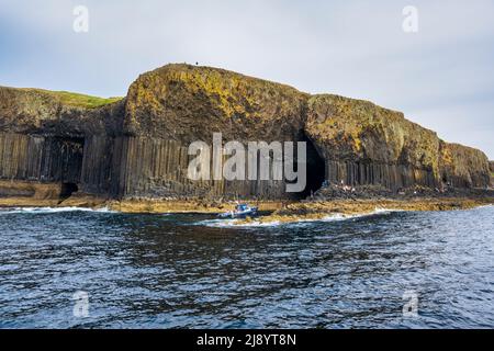 Un bateau touristique se trouve à l'entrée de la grotte de Fingal sur l'île de Staffa, dans les Hébrides intérieures, en Écosse, au Royaume-Uni Banque D'Images