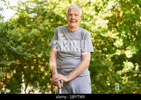 Vieil homme avec un bâton de marche après un accident vasculaire cérébral apprenant à marcher dans la clinique de réadaptation dans le jardin Banque D'Images