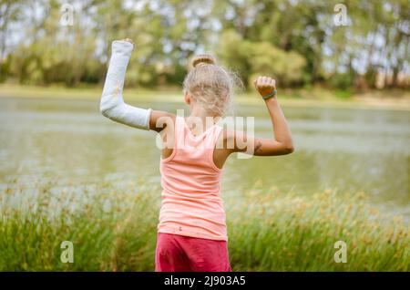 petit enfant avec bandage sur la main cassée debout vue arrière dans la nature verte au bord de la rivière Banque D'Images