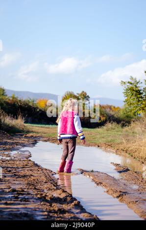 petite fille charmante qui profite d'une flaque d'eau après la pluie dans une atmosphère ensoleillée automnale saisonnière Banque D'Images