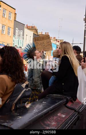 Londres punks avec une veste de lettre et de couleur bleue Liberty Spikes Mohawks sur la rue bondée ayant un bon moment tient une affiche, aider les punks à s'enivrer Banque D'Images