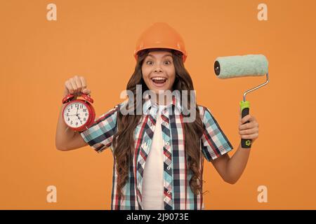 surprise adolescente tenir le rouleau de peinture et le réveil. enfant dans le casque. temps pour la décoration. Banque D'Images