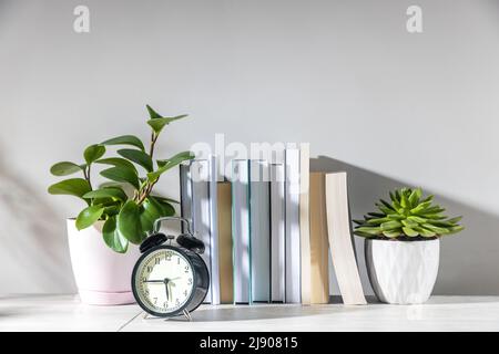 Peperomia magnoliifolia dans un pot en plastique rose, echeveria dans un pot en céramique, une pile de livres est sur la bibliothèque. Une chambre d'adolescent. Le réveil sh Banque D'Images