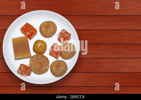 Variété de bonbons indiens sur une plaque blanche sur une table en bois. Vue de dessus Banque D'Images