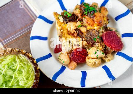 Gnocchi cuits avec betteraves en tranches sur une assiette rayée et un linge de table à carreaux, bol avec salade de concombre, gros plan. Banque D'Images