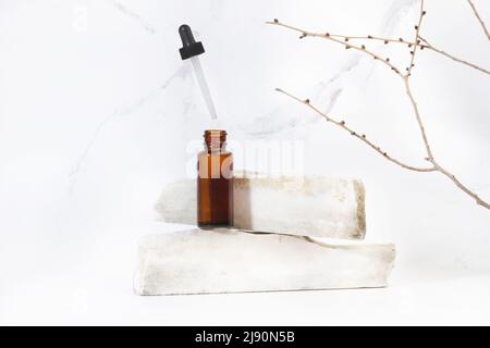 Une bouteille brune avec compte-gouttes sur des morceaux de marbre blanc sur fond blanc Banque D'Images