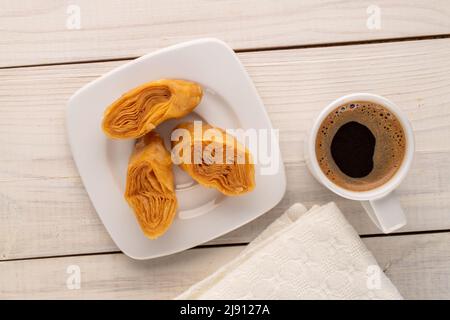 Trois morceaux de baklava au miel sucré avec une soucoupe en céramique blanche et une tasse de café sur une table en bois, vue rapprochée sur le dessus. Banque D'Images