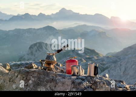 Cafetière Vaporing sur le poêle touristique et tasses en métal sur la pierre avec vue incroyable sur la montagne. Alpes juliennes, vallée de la Soca, Slovénie Banque D'Images