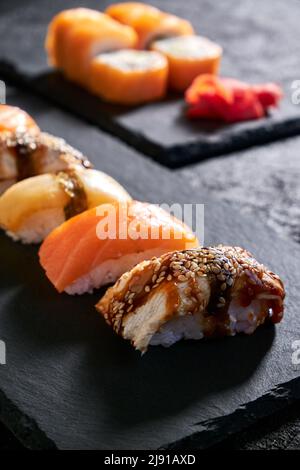 Assortiment de sushis au saumon, à l'anguille et à l'escolier sur une assiette en pierre noire sur fond sombre Banque D'Images