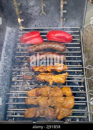 Barbecue de saucisses grillées fumées, satay de viande sur des bâtonnets et poivrons rouges coupés cuisant des plats à l'extérieur sur des charcoals chauds. Concept alimentaire. Banque D'Images