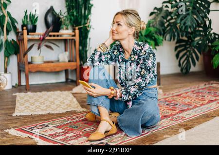 Jeune femme blonde décontractée assise sur le sol utilise le téléphone pour la communication en ligne. Banque D'Images