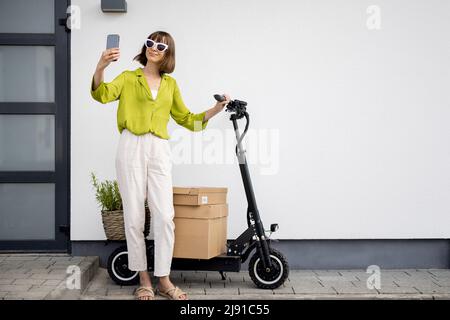 Femme parlant au téléphone tout en étant debout avec un scooter près de la maison Banque D'Images