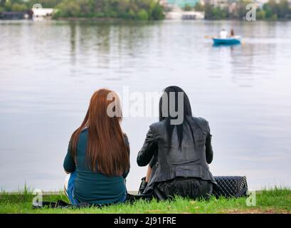 Vue arrière de deux filles assises sur le bord du lac Herestrau dans le parc du Roi Mihai I, Bucarest Banque D'Images