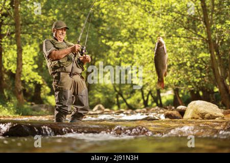 Pêcheur mature tirant un poisson de carpe hors d'une rivière dans le bois Banque D'Images