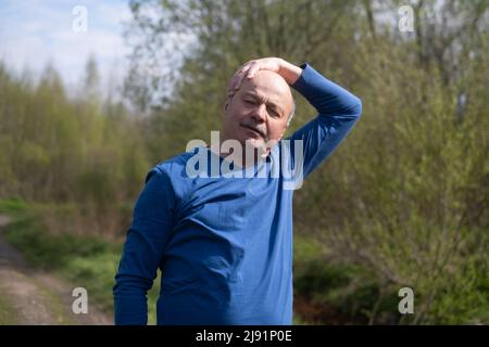 Coureur senior avec brassard faisant de l'exercice d'étirement. Nature printanière. Un mode de vie sain à la vieillesse. Banque D'Images