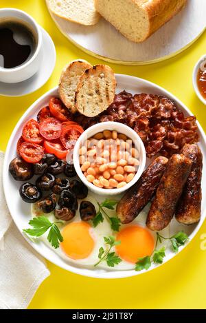 Petit-déjeuner anglais complet avec œufs frits, bacon, saucisses, haricots et champignons sur fond jaune. Banque D'Images