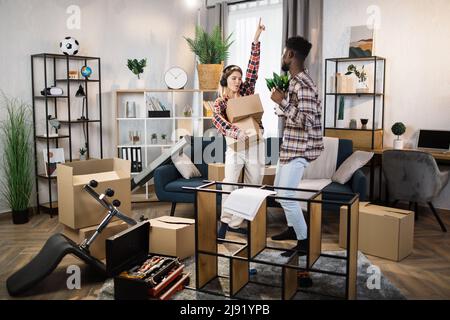 Joyeux couple multiracial dansant et écoutant de la musique dans le salon avec des boîtes en carton autour. Concept de réinstallation familiale, amusement et convivialité. Banque D'Images