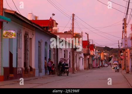 Scène de rue pittoresque après le coucher du soleil, pavés, mât télégraphique avec lignes électriques, personnes, Cubains debout devant la porte d'entrée, voiture, moto Banque D'Images