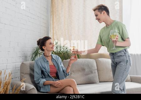 heureux homme de sexe féminin qui donne un verre de vin blanc à un partenaire assis sur un canapé Banque D'Images