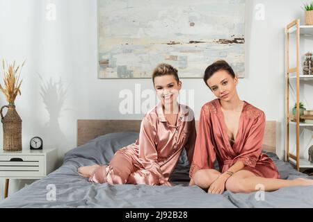 les jeunes amateurs de pansexués en sommeil sourient à la caméra tout en étant assis sur le lit Banque D'Images