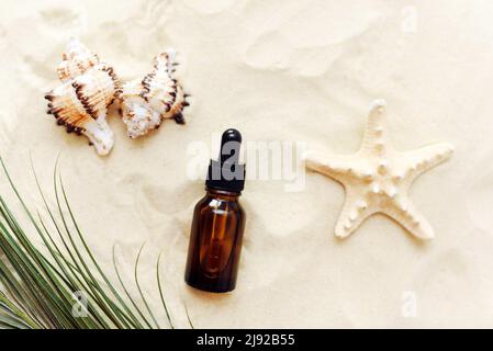 Une bouteille de sérum ou d'huile, un produit cosmétique dans une bouteille en verre avec une pipette sur fond de plage avec du sable. Présentation du produit sur fond sablonneux Banque D'Images