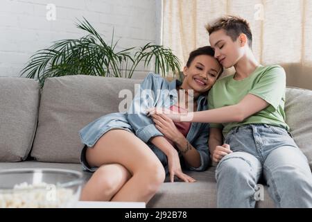 jeune bigender personne avec les yeux fermés assis sur le canapé près de partenaire gai Banque D'Images